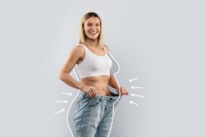 middle aged blonde woman wearing huge jeans, showing results of weight loss program