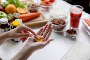 Woman holds vitamins next to nutritious foods on a dinner table for a healthier lifestyle.