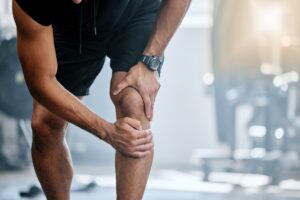 Man at the gym grips his knee in pain. Sound wave therapy can help to reduce inflammation and soreness.