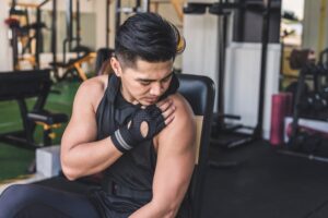 Young athletic man in the gym, looking at his sore arm and in need of PUR red light therapy.